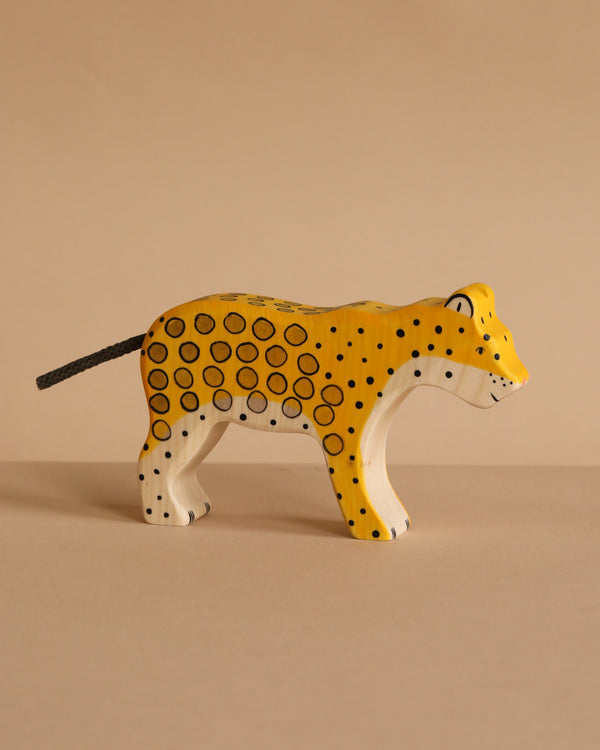 The Holztiger Leopard is a handcrafted wooden figure painted yellow with black spots and a white underside, shown standing on a beige surface against a beige background. Made in Europe.
