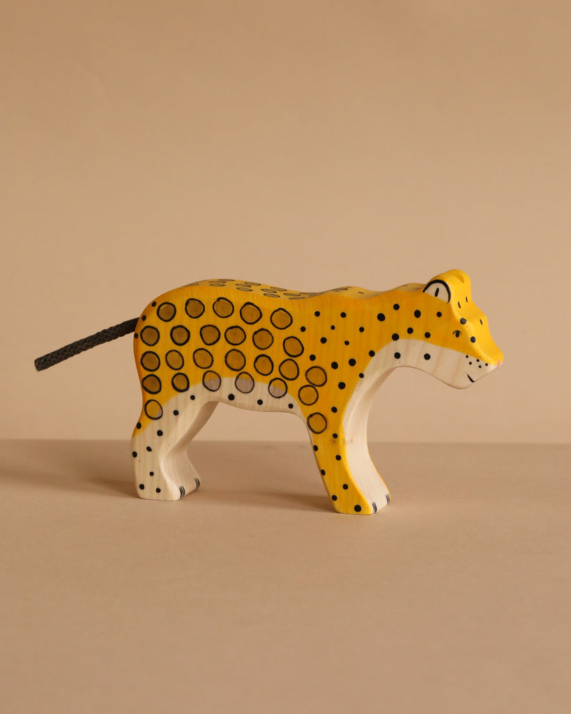 A handcrafted Holztiger Handmade Wooden Safari Animals Set leopard made of yellow wood, featuring painted black spots and a black string tail.