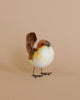 A handmade Wren Bird Stuffed Animal with a white and brown body, orange eye detail, and black metal feet, positioned against a soft peach background. This piece is part of our collection of hand-sewn animals.
