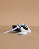 A pair of Minikane Doll Shoes | Converse Style Black Sneakers with white laces are displayed on a beige surface against a beige background.