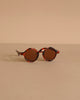 Minikane Doll Accessories | Harry Sunglasses feature round brown lenses and tortoiseshell frames, displayed on a beige surface—perfect stylish accessories for your Minikane doll.