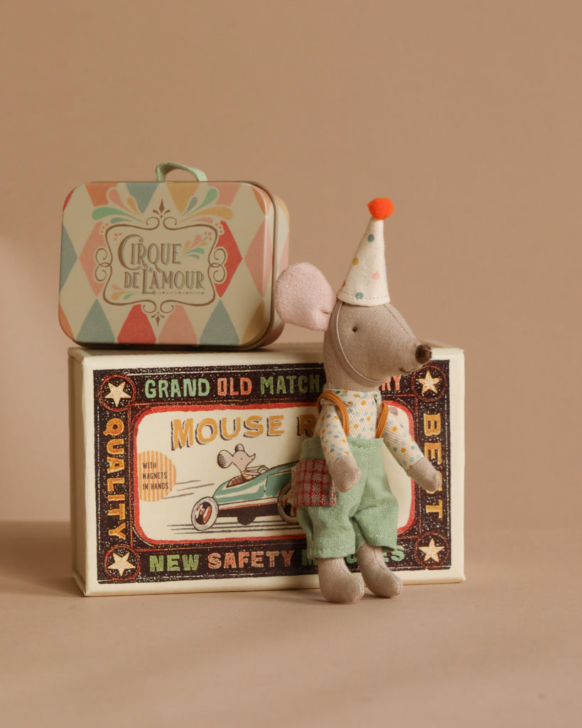 The Maileg Little Brother Mouse, dressed as a clown in teal overalls and a polka-dotted party hat, sits on a vintage-style matchbox beside a decorative suitcase displaying the retro text "Cirque de l'amour.