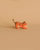 A small handcrafted wooden figurine of an orange tiger with black stripes and a rope tail, named Ostheimer Tiger Lurking, Small, is placed against a beige background. The toy appears to be in a crouching or playful position, perfect for imaginative play.
