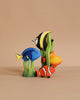 The Bumbu Handmade Wooden Tropical Fish Set features four colorful painted wooden fish—blue, yellow-black-white, orange, and yellow—standing among green plants on a beige background. Perfect addition to any Montessori toy collection.