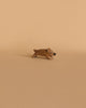 A small, light brown wooden figurine of a wild boar in a playful stance, handcrafted by Ostheimer, placed on a beige background.