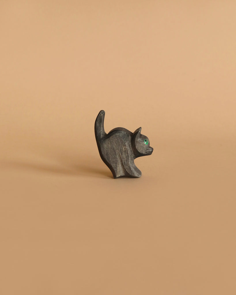 A small, dark brown wooden witch figurine with green eyes stands on a tan background. This whimsical piece, crafted in the style of Ostheimer toys, features an arched back and raised broom. It's been lovingly made from sustainably sourced materials.