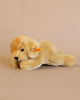 A Steiff Golden Retriever Dog Stuffed Animal, identifiable by the Button in Ear trademark, is lying on its side against a plain beige background. The stuffed animal has soft, realistic fur texture and blue eyes.