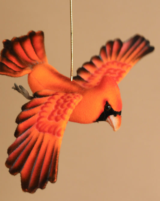 The Cardinal Flying Bird Stuffed Animal, a plush red ornament with outstretched wings, hangs from a string against a neutral background.