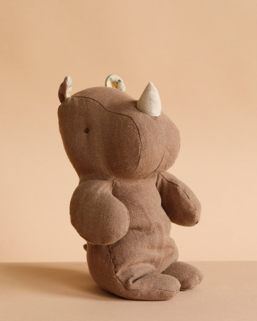 The Maileg Small Rhino - Chocolate, crafted from soft fabric and recycled polyester, sits upright on a neutral beige background—perfect for joining your Safari friends collection.