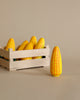 A wooden crate filled with several Erzi Corn on the Cob Pretend Foods with a prominent yellow and white patterned cob standing upright in front of it on a plain background.