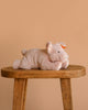 The Steiff Piko Pig Plush Toy, 11 inches, features soft light pink fur and a small orange bow on its ear. It rests on a wooden stool against a beige background—an adorable addition to any stuffed animal collection.