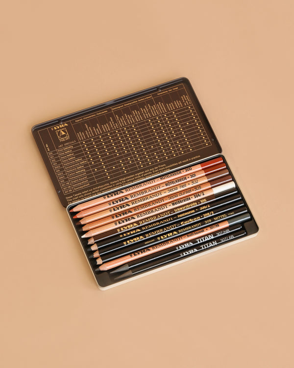 The Lyra Rembrandt Fine Art Special Pencils set contains 12 assorted dry and oil pencils, neatly packed in a metal tin with a gold chart on the inside lid, displayed against a beige background—perfect for artists.
