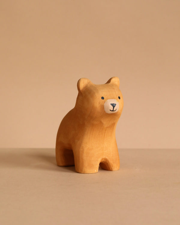 The Bumbu Handmade Wooden Curious Bear, a small, hand-carved toy with a painted face, rests on a neutral beige surface against a matching beige background.