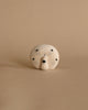 A whimsical handcrafted wooden sculpture of a stylized face with multiple simple eyes and a central nose, set against a plain beige background.