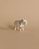 A small Tiny Wooden Zebra figurine with distinct black stripes on a beige background. The zebra is facing left and stands in a neutral posture.