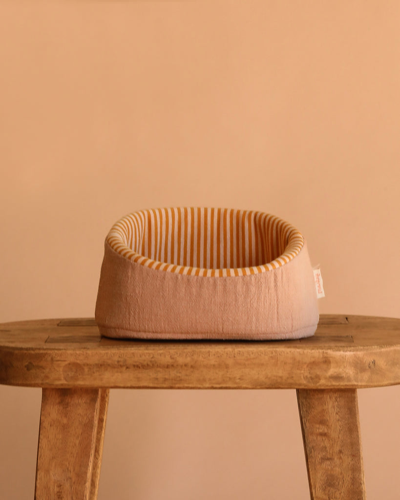 The Maileg Small Sleeping Kitten in Basket features a small, round beige basket with yellow and white striped lining, ideal for display or pairing with other Maileg accessories against a neutral background.