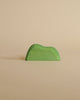 A small, green, minimalist handcrafted Ostheimer Bush shaped like a hill, placed against a plain beige background.