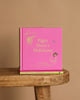 A pink hardcover of "Winnie-the-Pooh: Piglet Meets A Heffalump" sits upright on a wooden stool with another copy flat underneath, against a plain beige background—ideal for fans of classic bedtime stories and Winnie the Pooh.