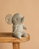 The Maileg Elephant, Small - Iron Grey, with soft plush and patterned ears, sits charmingly on a wooden bench against a beige background—a cute addition to any Safari friends collection.