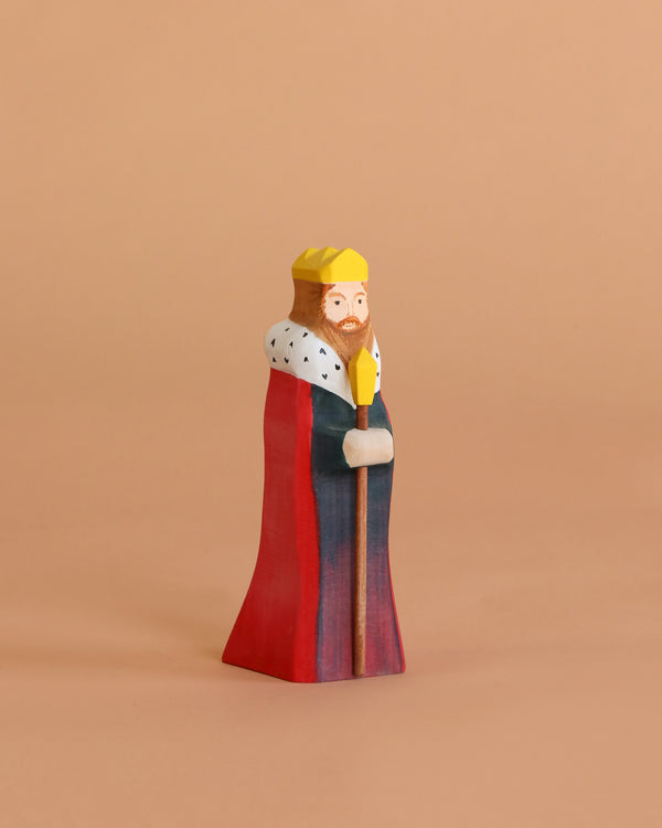 The Bumbu Handmade Wooden King, wearing a yellow crown and colorful robe with a scepter, stands against a beige background—ideal for medieval-themed playsets.