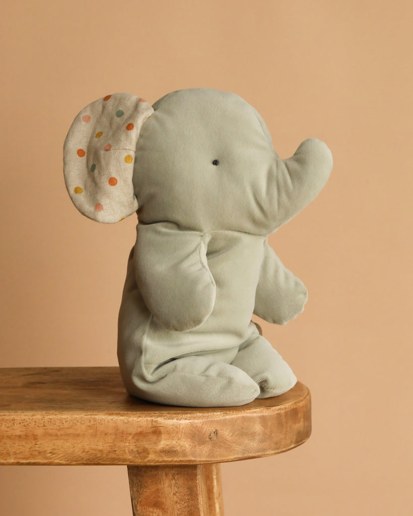 The Maileg Elephant Soft, Medium - Iron Grey, is a charming light gray stuffed toy made from recycled polyester plush. Sitting upright with polka-dotted inner ears, it adds a delightful touch to any space.