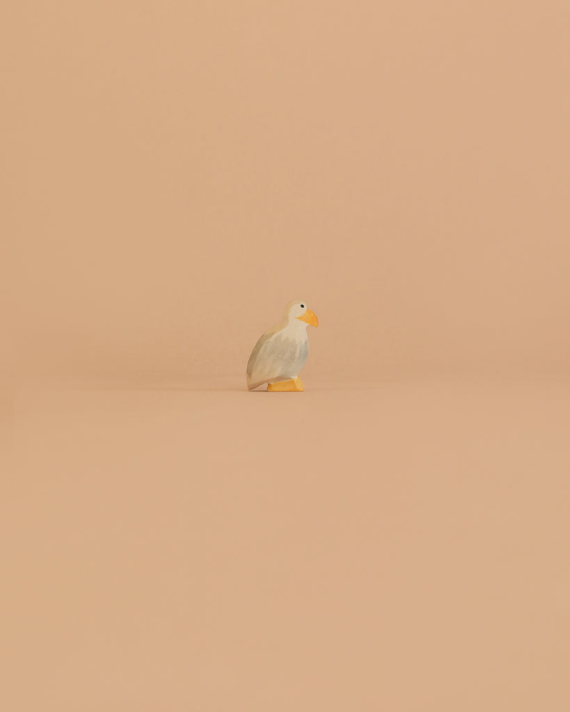 The Ostheimer Bird - Bald Eagle, Small stands alone on a smooth, peach-colored surface with a matching background, capturing the charm of handcrafted toys.