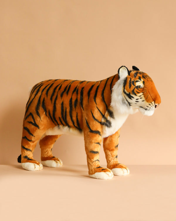 The Ride-On Tiger is a handcrafted plush large toy with orange fur, black stripes, and white accents, standing on a beige surface against a matching background and showcasing realistic features.