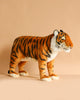 The Ride-On Tiger is a handcrafted plush large toy with orange fur, black stripes, and white accents, standing on a beige surface against a matching background and showcasing realistic features.