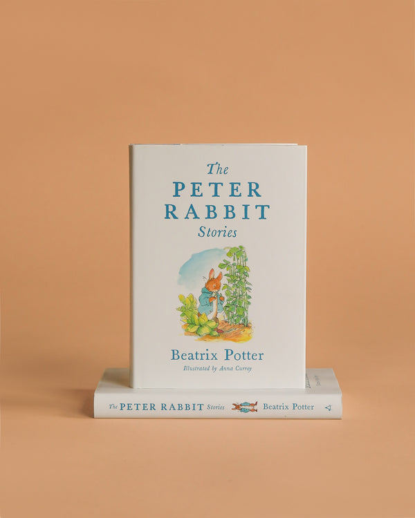 A book titled "Peter Rabbit Stories: Deluxe Edition With New Illustrations" stands upright on an orange background, its cover featuring Peter Rabbit. Another copy lies flat beneath it, showcasing the charm of this beloved classic.