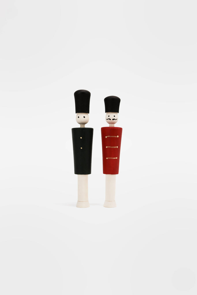 Two Wooden Soldiers, featuring uncomplicated facial features, stand together like cheerful guardians. One is dressed in black, while the other sports a red ensemble with gold highlights. Both are topped with tall black hats against a plain white background, making them ideal for adding charm to an advent calendar.