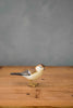 The Hand Carved Ornament - Sparrow Bird - 3.5"H features lifelike brown, white, and black markings on sustainable softwood. This small figurine captures nature’s charm and stands out against a plain gray background.