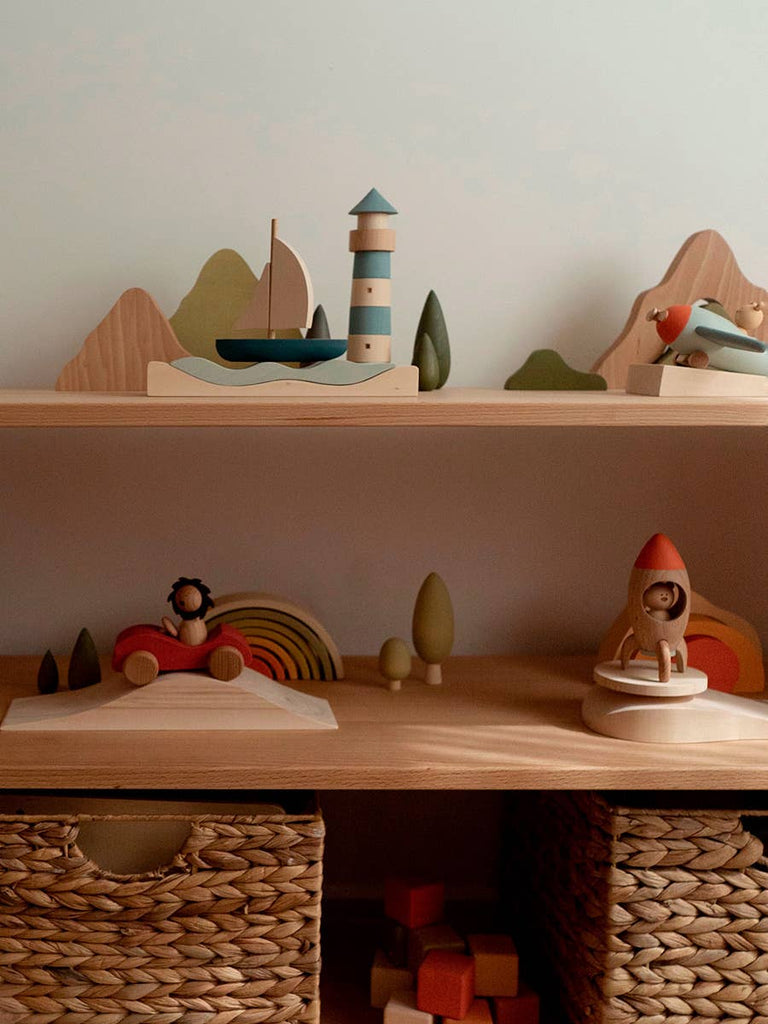 A collection of wooden toys on two shelves, featuring a Sabo Concept Lighthouse, a sailboat, a toy car, and a rocket ship for maritime adventure play.