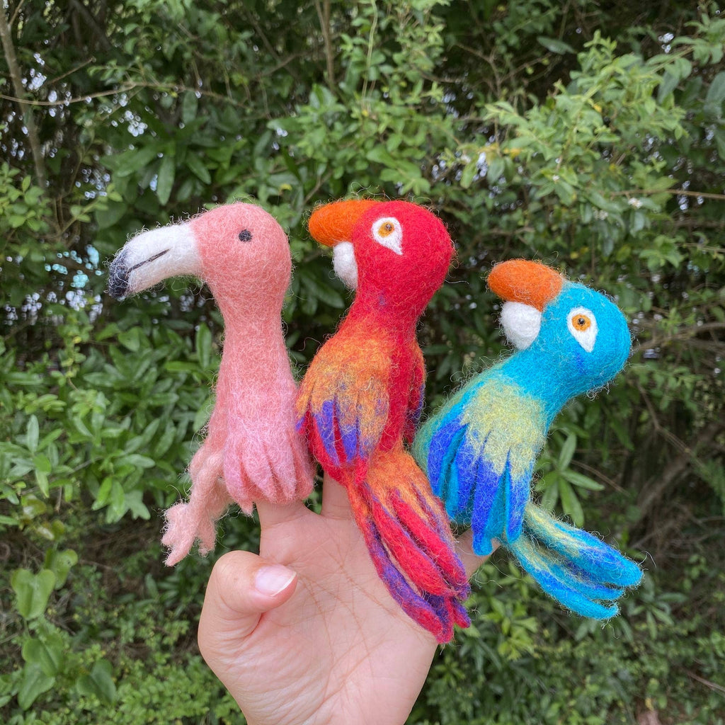 A hand holds three colorful, needle-felted finger puppets—including the Flamingo Finger Puppet—perfect for imaginative play, with green foliage in the background.