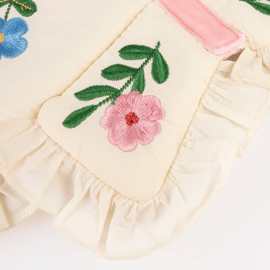 Close-up of Meri Meri Butterfly Wings in cream-colored natural cotton with ruffled edges, embroidered pink and blue flowers, green leaves, and a pink velvet ribbon accent.