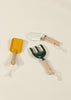 The Gardening Tools Playset features three kids' tools with light wooden handles and white cord loops—a yellow trowel, a white trowel, and a green hand rake—arranged on a beige background, ideal for educational play.