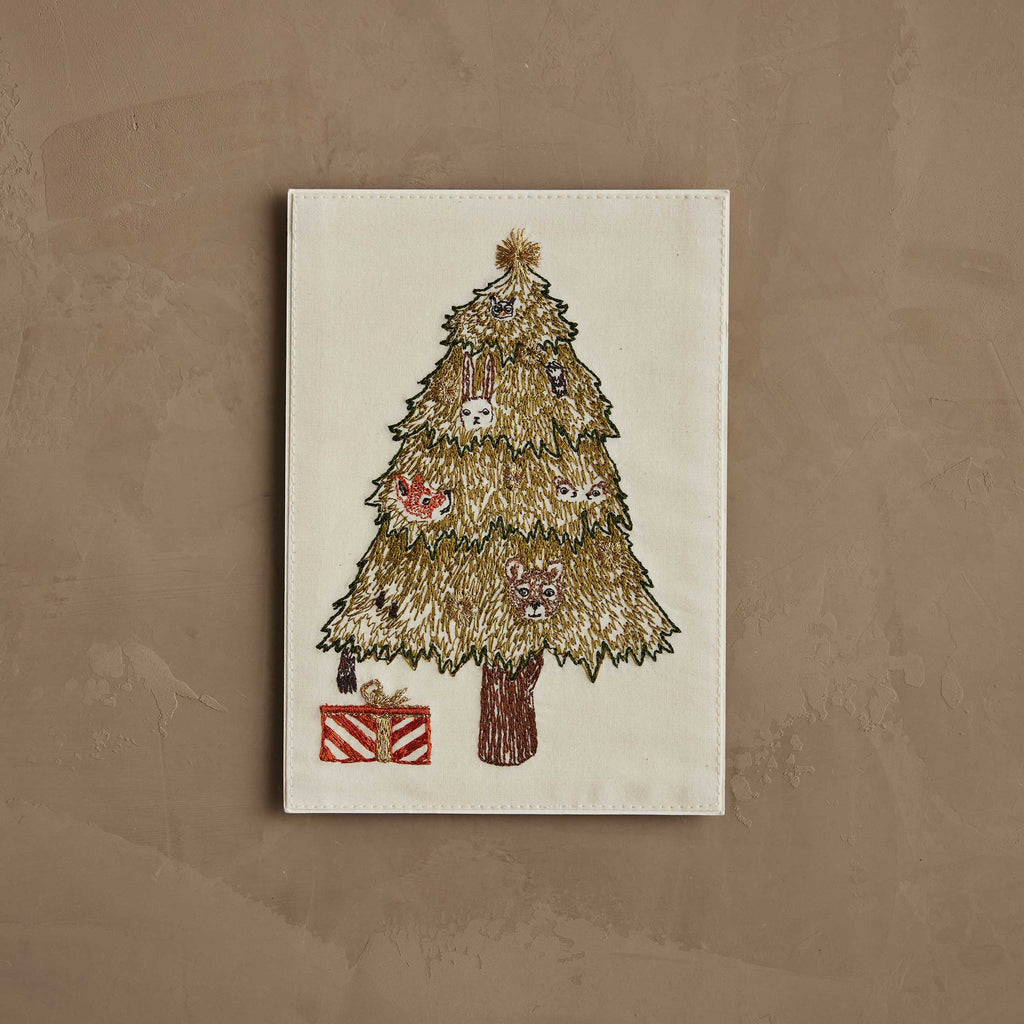 The Coral & Tusk Peek a Tree Card is an embroidered keepsake featuring a Christmas tree with a bunny, fox, bear, and owl peeking through the branches and a red and white striped gift beneath on a plain beige background.