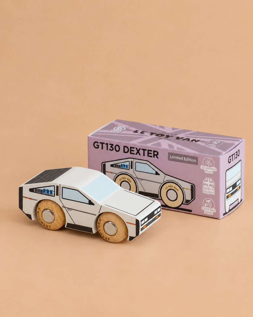 A sleek white wooden toy car with black detailing, the No. 23 GT130 Dexter | Made in England, sits in front of a purple box on a beige surface. The box displays an illustration matching this modern collectible and is labeled “GT130 DEXTER Limited Edition,” inviting young drivers to embark on imaginative adventures with this futuristic wooden car.