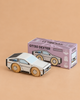 A small, modern wooden car—No. 23 GT130 Dexter | Made in England—sits beside its purple box on a beige surface, perfect for imaginative play.