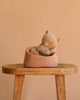 The Maileg Small Sleeping Kitten in Basket features a plush kitten with closed eyes resting in a round, peach-colored basket on a wooden stool, set against a beige background—an ideal match for Maileg accessories.
