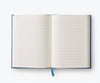 The Menagerie Garden Embroidered Journal, an open, blank lined keepsake with a blue ribbon bookmark, lays flat on a white background.