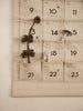 A Ferm Living Star Christmas Calendar - Sand/Black canvas calendar with 24 numbered pockets, decorated with a pinecone branch and two small mushroom ornaments.