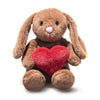 Steiff Hoppie Rabbit – Love is a brown plush bunny with long ears, a pink nose, and black stitched eyes. It sits upright holding a red heart-shaped pillow—a charming gift for Steiff fans. Background is plain white.