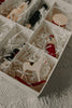 The Sabo Concept Christmas Ornaments set includes festive, hand-painted wooden figures—a white rocking horse, drum, nutcracker, and a red-clad figure—in a compartmentalized white box filled with white shredded paper.