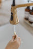 A hand holds a Winnie-the-Pooh: Pooh’s Birthday Surprise (Water Reveal) book under running water from a kitchen faucet.