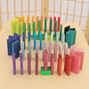 Grimm's Color Charts-Rally features vibrant dominoes arranged upright in concentric circles on a light wooden surface, showcasing a blue, green, yellow, red, and pink gradient with light wood panels as the backdrop.
