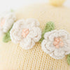 Close-up of Cuddle + Kind Flora the Duckling - Ivory: knitted yellow fabric with white and pale pink crocheted flowers and green leaves, echoing heirloom doll textures.