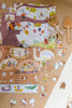 The Beneath the Branches 200 Piece Puzzle with animal characters lies partially assembled on wood beside a plush mouse and two wooden utensils. Matte pieces, some loose, are scattered near the edge of a white rug.