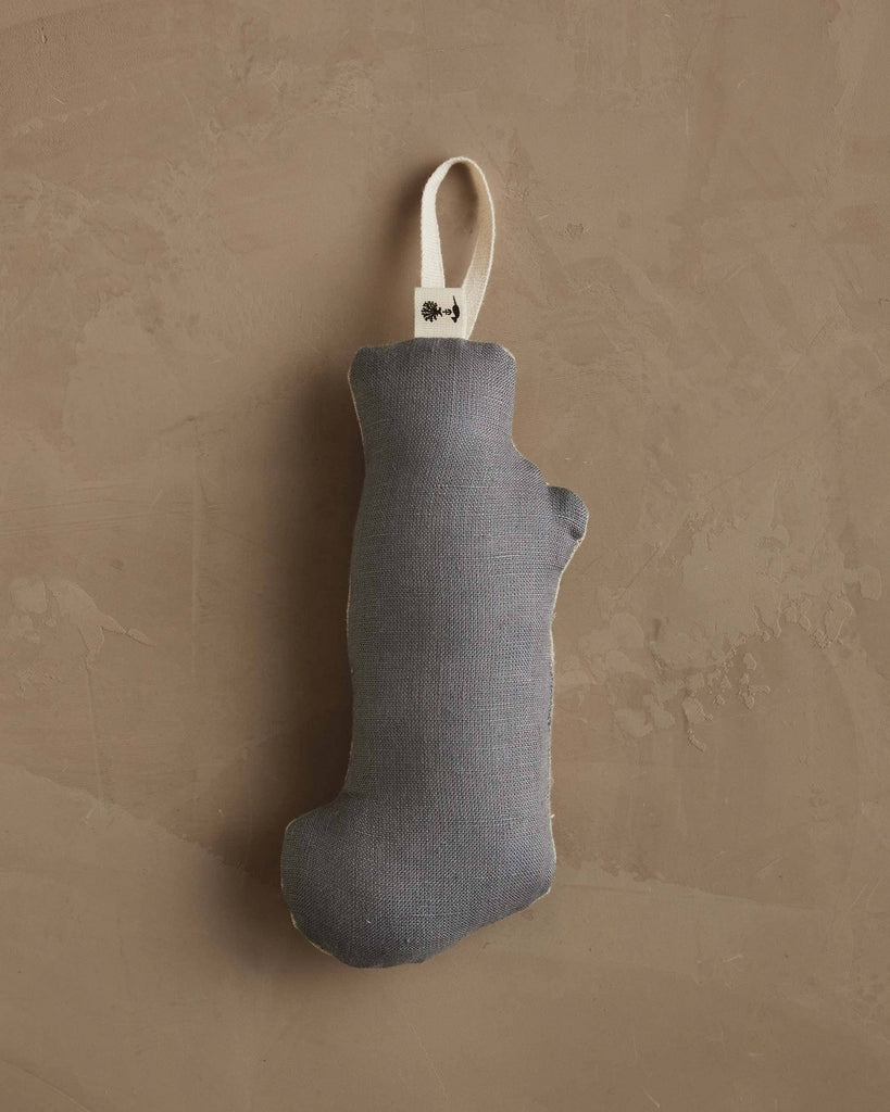 The Coral & Tusk Puppy Stocking Ornament, a small gray Michigan-shaped fabric Christmas stocking with a cream loop for hanging, is displayed against a textured brown wall.