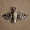 The Coral & Tusk Bat Surprise Doll, featuring fabric bat wings, embroidered accents, and a neutral palette, hangs against a textured beige wall.