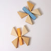 Two butterfly shapes made from wooden blocks on a white surface. Each butterfly, part of the Pastel Duo Block Set, consists of four geometric triangular wings and a rectangular body—one with a blue body and the other with an orange body.